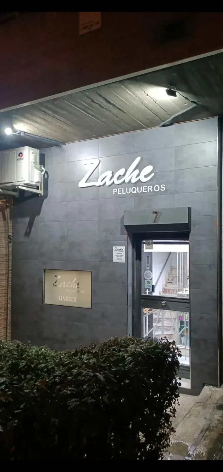 Fachada iluminada de Zache Peluqueros en la calle Javier de Miguel